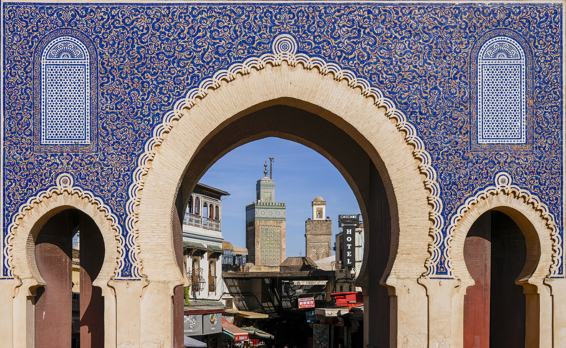 The blue-tiled arches of Bab Bou Jeloud gate framing the green minaret of a mosque in the Fes medina, Morocco