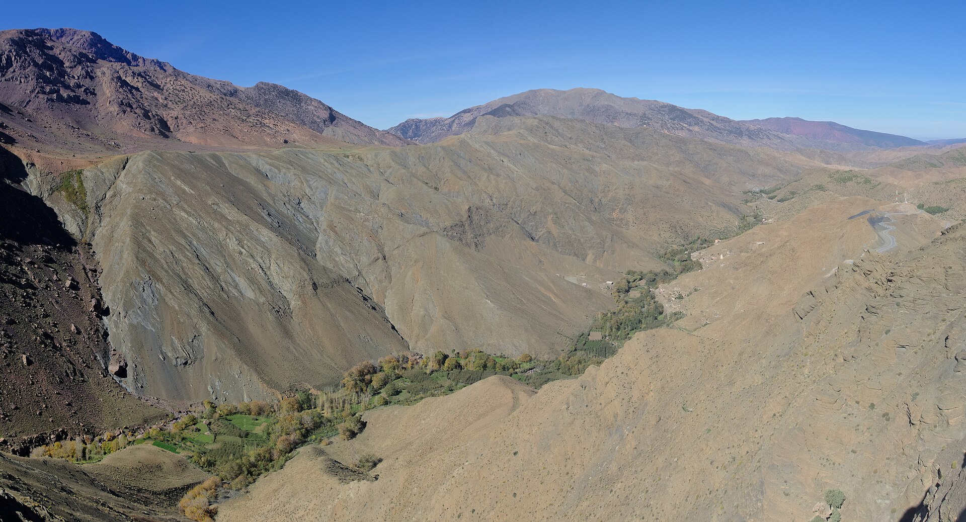 An elevated view of the Tizi n'Tichka mountain pass road switchbacking along a ridge in Morocco's High Atlas Mountains, overlooking a green valley oasis